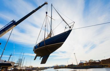 Zeilboot wordt met een hijskraan uit het water getild bij een scheepswerf