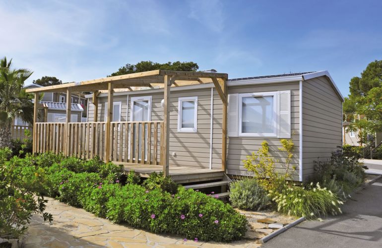 Stacaravan met houten veranda en beplanting op een vakantiepark